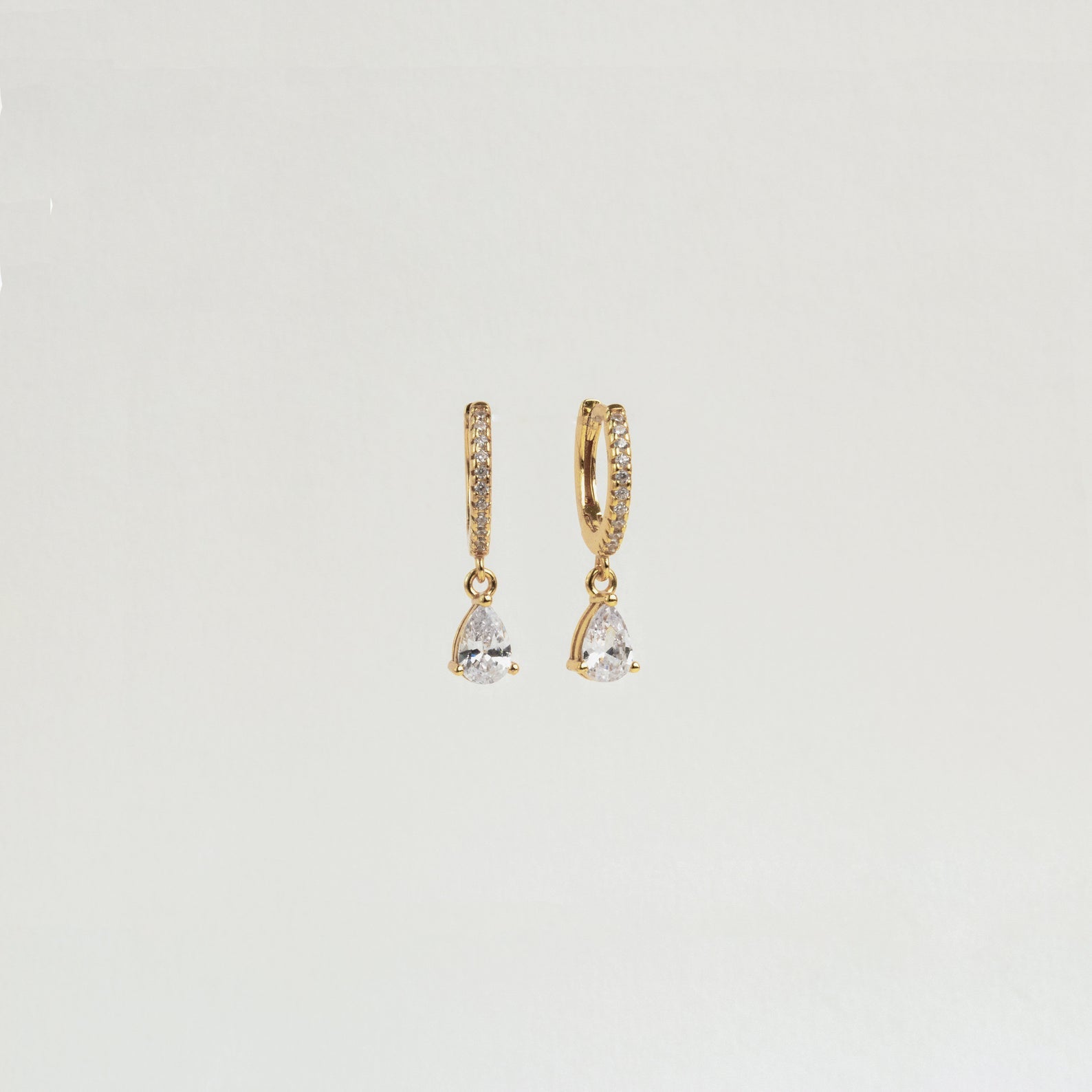 Diamond Drop Huggies with small clear teardrop-shaped gemstones elegantly hang from each earring, styled as semi-formal accessories on a plain white background.