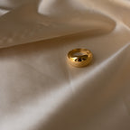 The Bold Dome Ring shines atop smooth beige satin fabric, its golden surface highlighted by gentle folds and soft lighting.