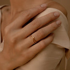 A hand wearing the Curve Stacking Set rests on a bare shoulder, complemented by a cream satin garment. The thin gold bands add subtle elegance to the look.