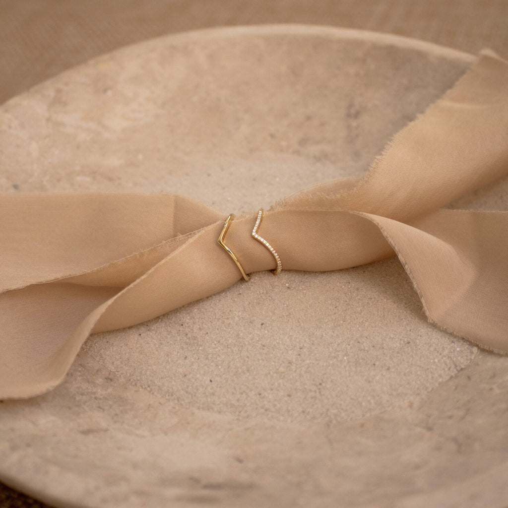 Two Curve Stacking Set rings rest on beige fabric atop a round, textured plate—ideal for creating a delicate stack with thin bands.