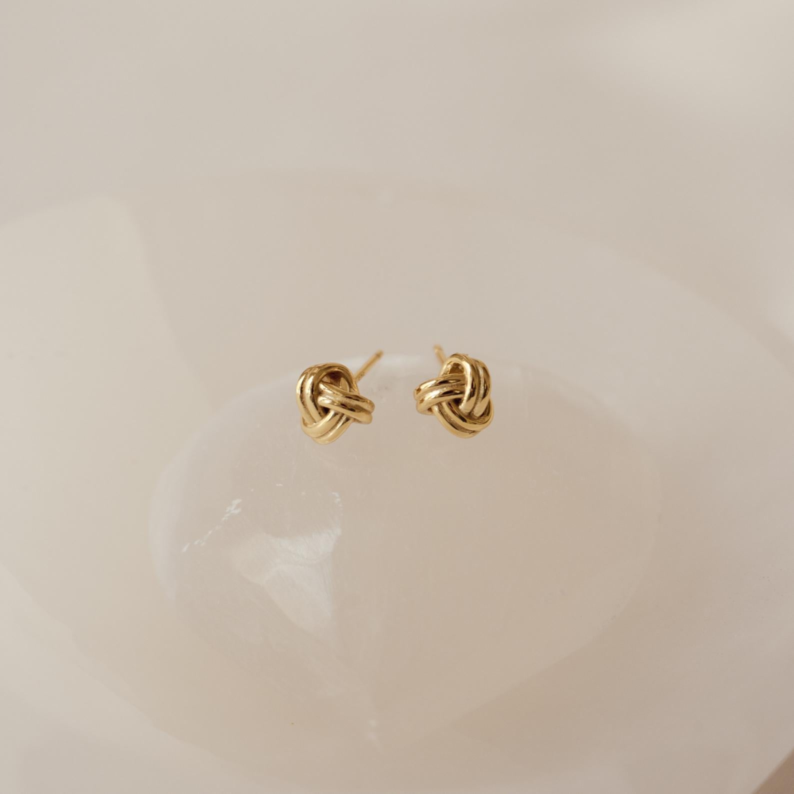 Love Knot Studs in Sterling Silver are shown on a smooth, light-colored stone background—these symbolic earrings make a perfect unity gift.