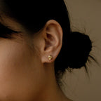 Close-up of a woman's ear wearing Love Knot Studs, small gold earrings symbolizing love—perfect as a thoughtful gift. Her dark hair is tied in a low bun.