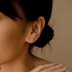 A woman with dark hair in a bun wears Love Knot Studs, elegant and symbolic jewelry, her hand gently placed near her neck.