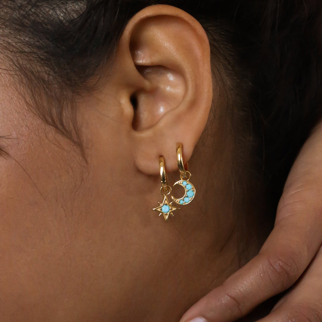 Close-up of an ear wearing the Boho Turquoise Earring Set, featuring gold hoops with star and blue crescent moon charms for a bohemian vibe.