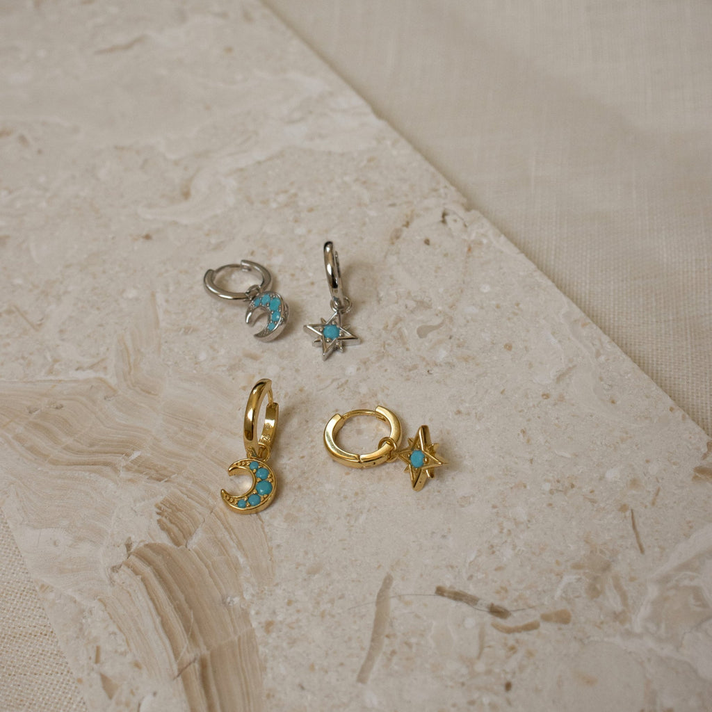 The Boho Turquoise Earring Set features four small gold and silver earrings with moon and star designs and turquoise stones, displayed on a textured beige surface—perfect for lovers of turquoise jewelry.