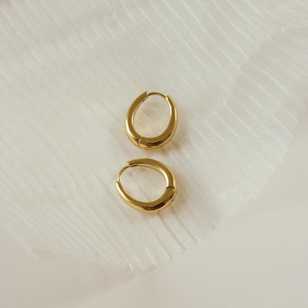 The Paris Oval Hoops earrings are displayed on a textured white fabric background.