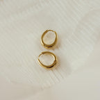 The Paris Oval Hoops earrings are displayed on a textured white fabric background.