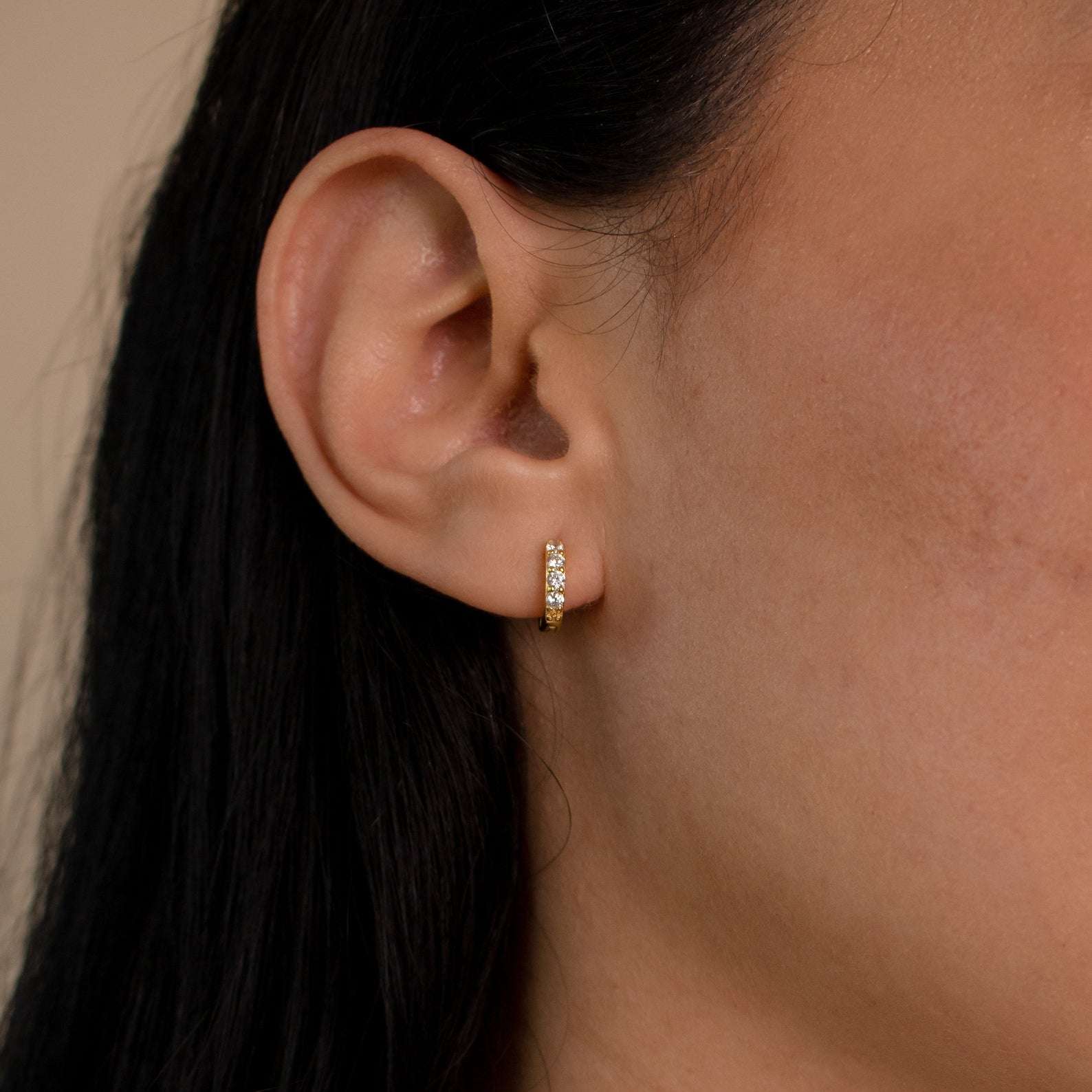 Close-up of a person's ear wearing Elise Diamond Huggies in 18K Gold—small gold hoops with white stones, ideal for an elegant everyday look.