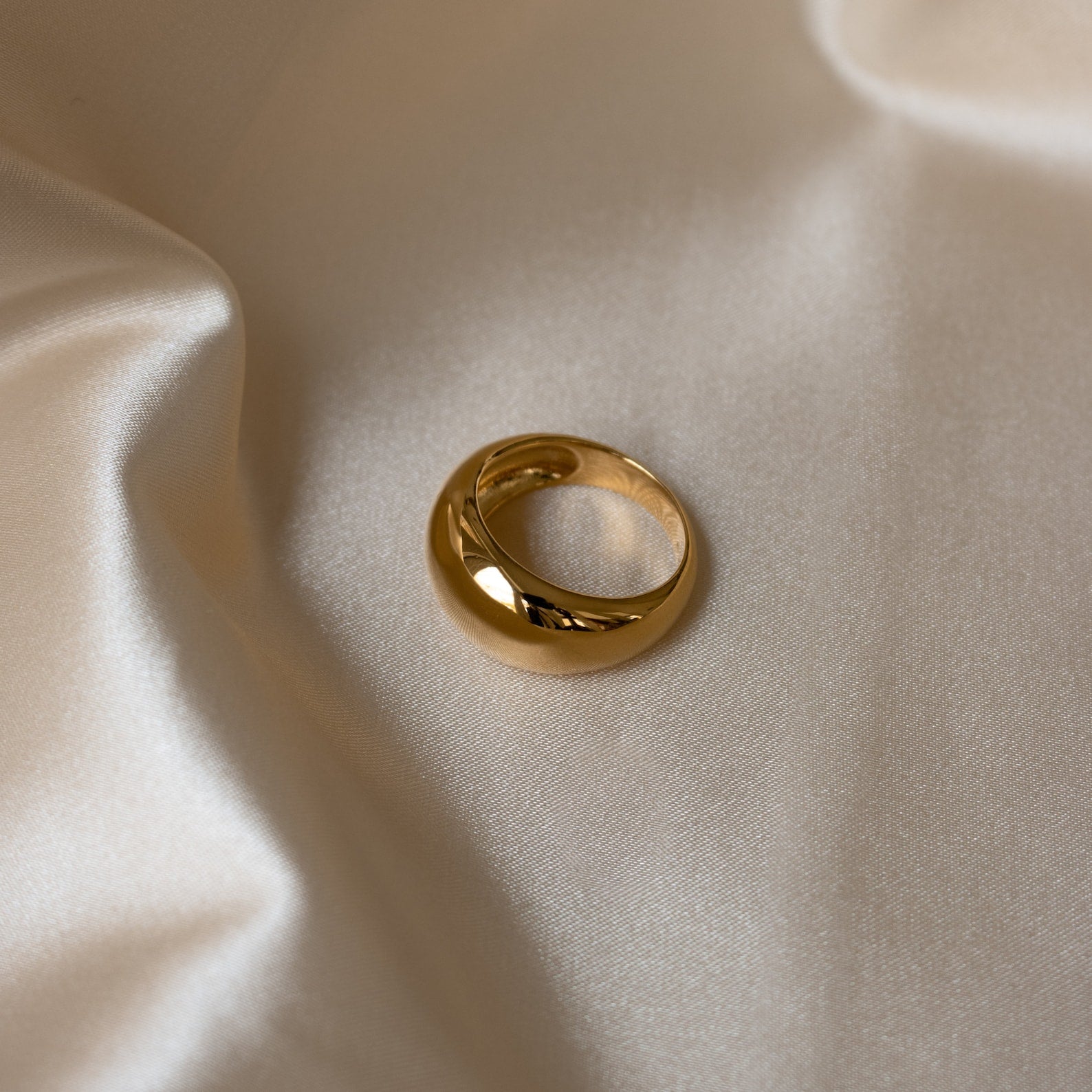 The Bold Dome Ring shines elegantly as it rests on smooth, cream-colored satin fabric.