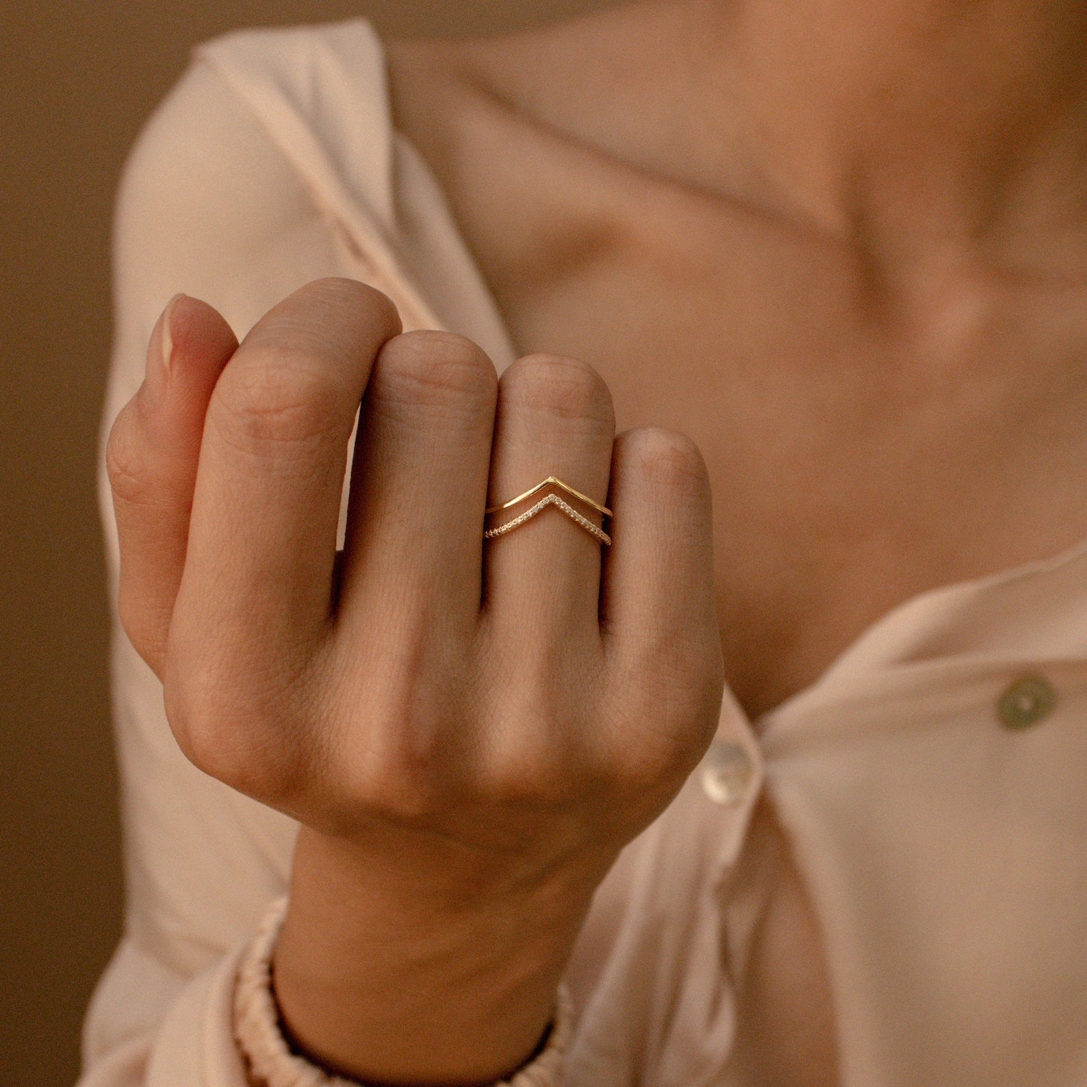 A person wearing a gold ring from the Curve Stacking Set on their finger, dressed in a light, partially unbuttoned blouse.