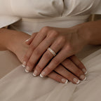 Close-up of hands with French manicured nails wearing the Colette Eternity Ring, an opulent gold band set with baguette diamonds, resting on a white dress.