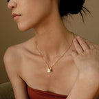 Woman wearing the Padlock Paperclip Necklace with a gold lock pendant, touching her collarbone while dressed in a strapless top.
