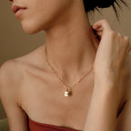 A woman touches her neck while wearing the Padlock Paperclip Necklace, featuring a gold pendant engraved with N.K.