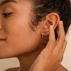 Jady Wire Diamond Hoops in 18K gold worn on ear with hand gently touching earlobe, showcasing delicate diamond pave setting.