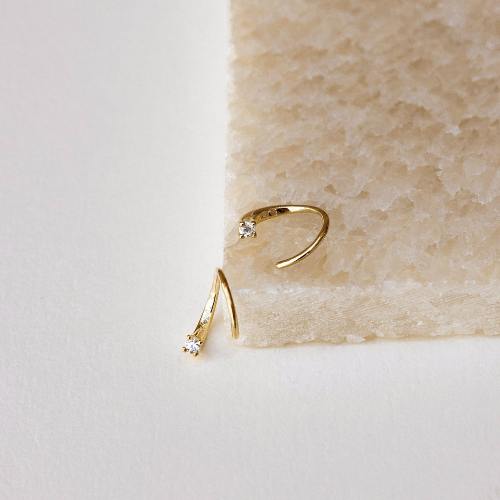 Jady Wire Diamond Hoops in 18K gold with delicate pavé diamonds on thin wire hoops displayed on beige textured surface and.