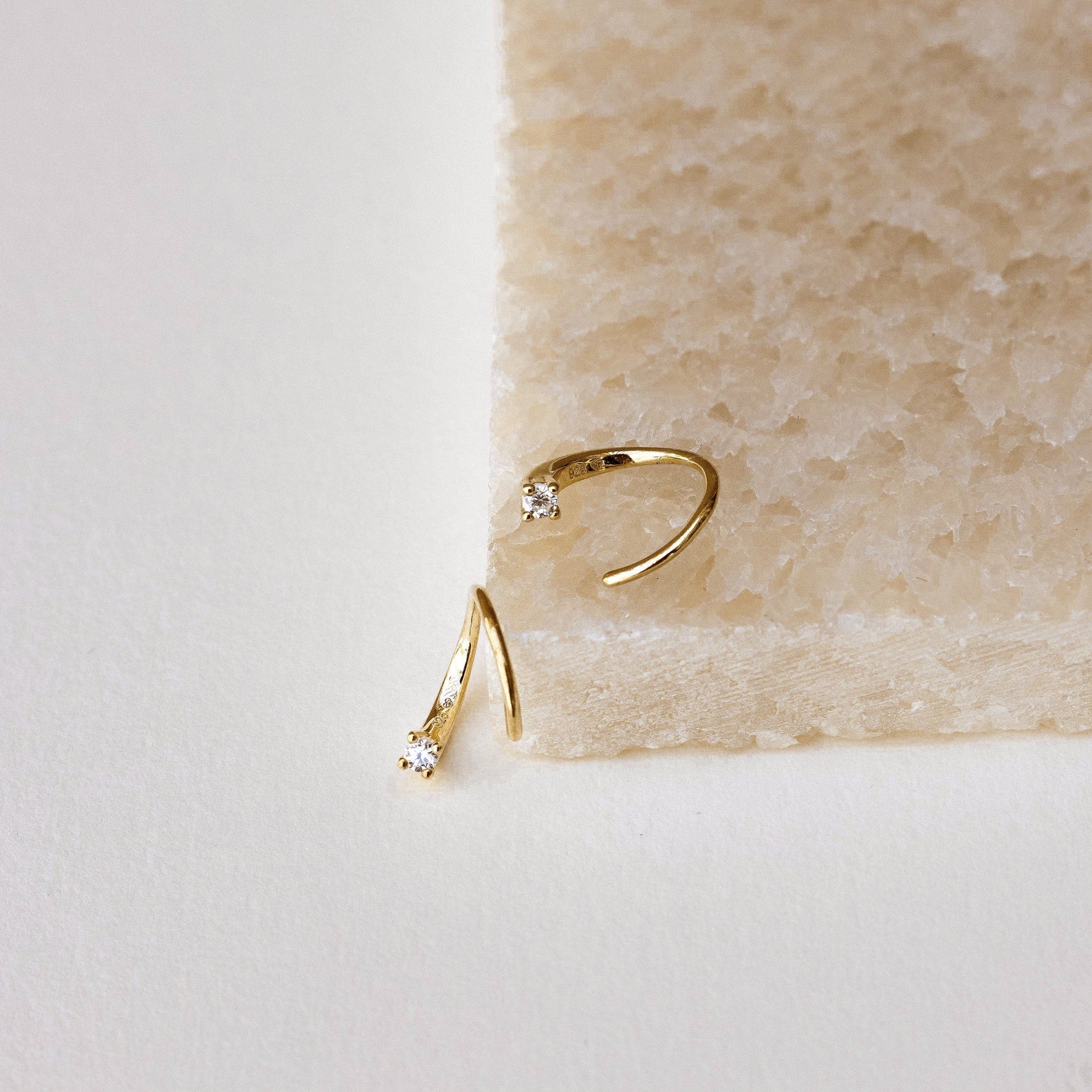 Jady Wire Diamond Hoops in 18K gold with delicate pavé diamonds on thin wire hoops displayed on beige textured surface and.