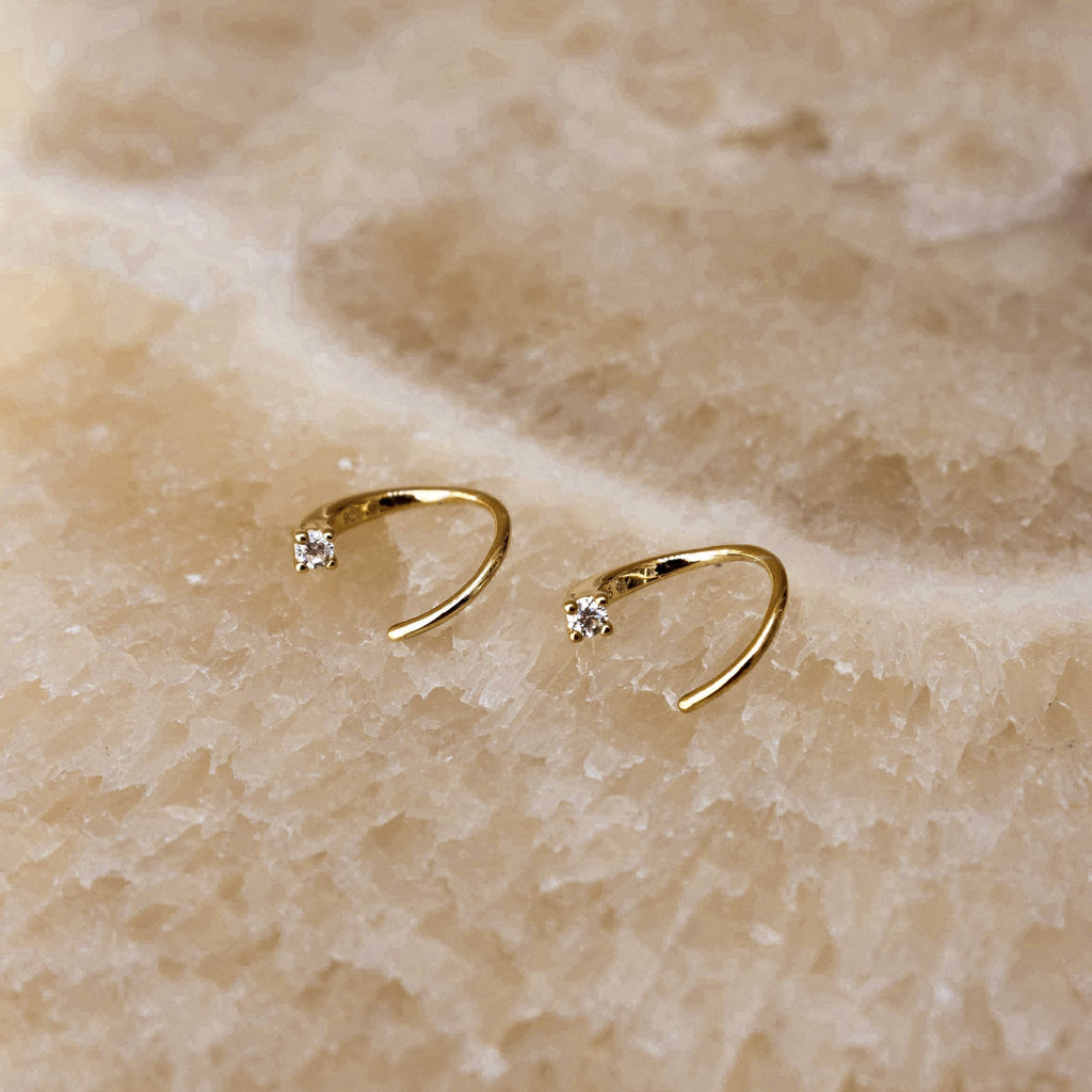 Jady Wire Diamond Hoops in 18K gold with single small round diamond on each delicate open hoop resting on textured beige.