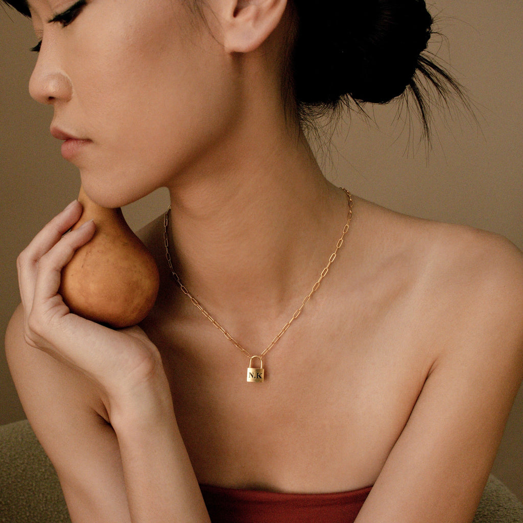 A woman with short hair holds a pear and wears the Padlock Paperclip Necklace, looking to the side.