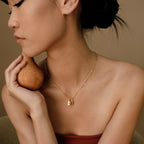 A woman with short hair holds a pear and wears the Padlock Paperclip Necklace, looking to the side.