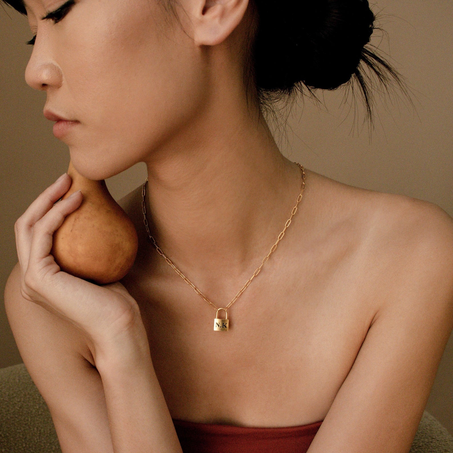 A woman with short hair holds a pear and wears the Padlock Paperclip Necklace, looking to the side.