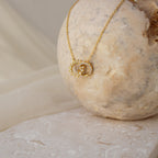 The Sun  Moon Eternity Necklace features celestial charms, elegantly displayed on a round beige stone with a soft neutral background.