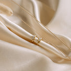 The Giana Marquise Huggies, two gold rings with clear gemstones, rest elegantly on soft beige satin fabric.