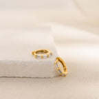 Gold hoop earrings with clear embedded stones on a beige fabric background