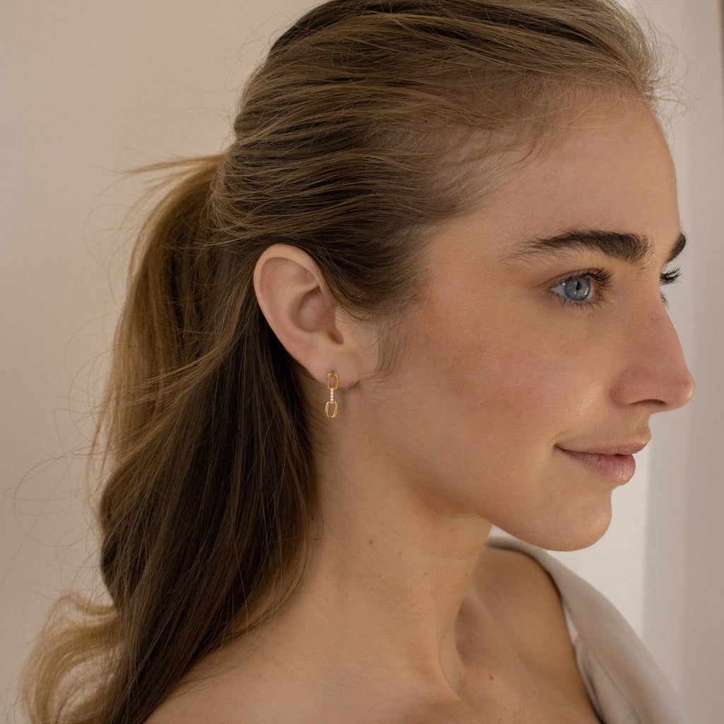 A woman with light brown hair in a ponytail wears the Linked Earrings Set from her jewelry collection, looking to the right and smiling softly.