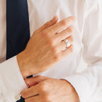 A man in a white shirt and dark tie adjusts his cuff, showcasing the Thick Handwriting Band—a minimalist statement ring engraved with text.