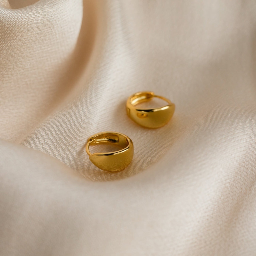 Two Olivia Hoops earrings are displayed on smooth, light beige satin fabric with gentle folds, bringing a modern touch to any outfit.