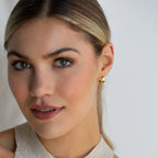 A blonde woman with light eyes wears Olivia Hoops earrings and a beige sleeveless top, facing the camera for a modern look.