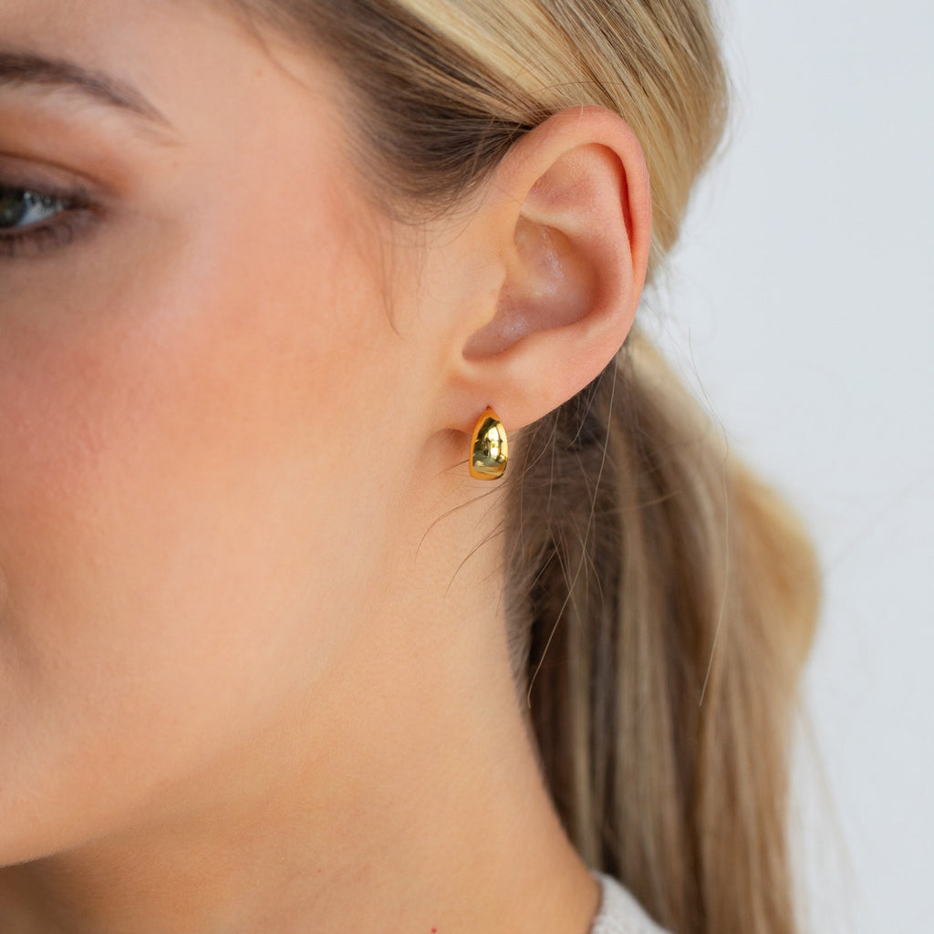 Close-up of a woman's ear adorned with Olivia Hoops, shiny gold earrings that add a contemporary touch to her style.