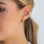 Close-up of a woman's ear adorned with Olivia Hoops, shiny gold earrings that add a contemporary touch to her style.