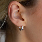 Close-up of a person’s ear wearing Olivia Hoops in Sterling Silver—small, shiny hoop earrings that refresh classic style with a contemporary touch.