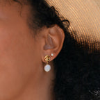 Close-up of a woman's ear wearing Knot Pearl Drop Earrings—featuring gold knots with pearl drops—and a small stud above, ideal for those who appreciate minimalist style.