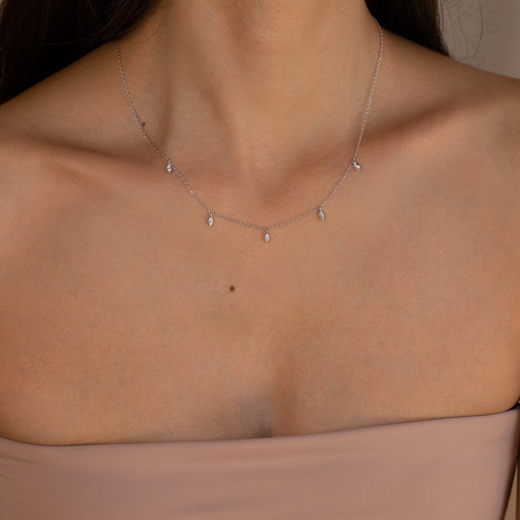 A woman wearing the Marquise Station Necklace, featuring marquise-shaped stones as delicate charms on a dainty chain, paired with a strapless nude top.