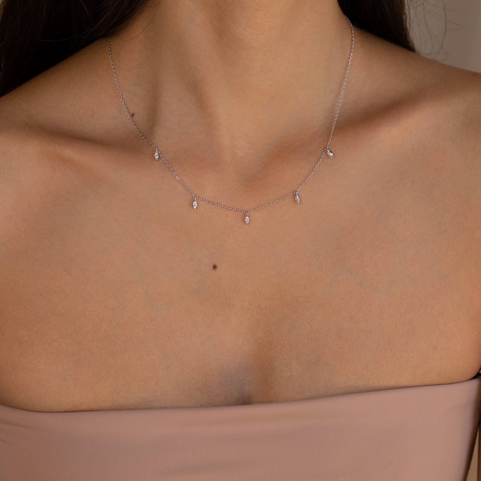 A woman wearing the Marquise Station Necklace, featuring marquise-shaped stones as delicate charms on a dainty chain, paired with a strapless nude top.