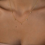 The Marquise Station Necklace gently drapes along a woman's neck and collarbone, featuring a dainty gold chain accented with marquise diamonds and dangling teardrop charms for an elegant look.