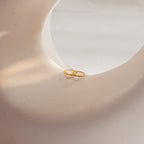 The Pave Cartilage Mini Huggies in 18K Gold rest on a smooth, curved white surface bathed in soft natural light, highlighting their timeless elegance.