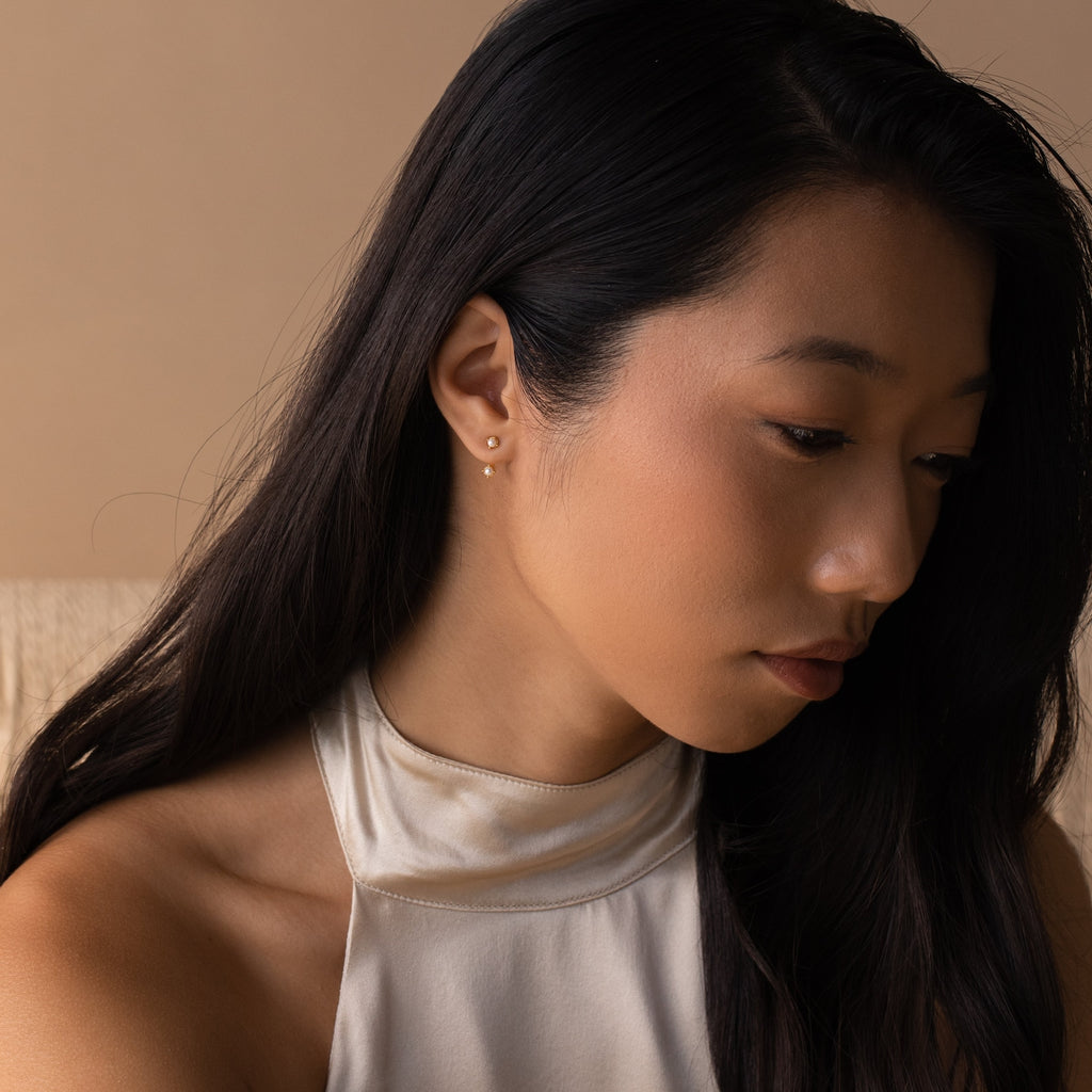 Lifestyle portrait of a woman wearing one birthstone pearl ear jacket in her lobe, styled with a white halter top.