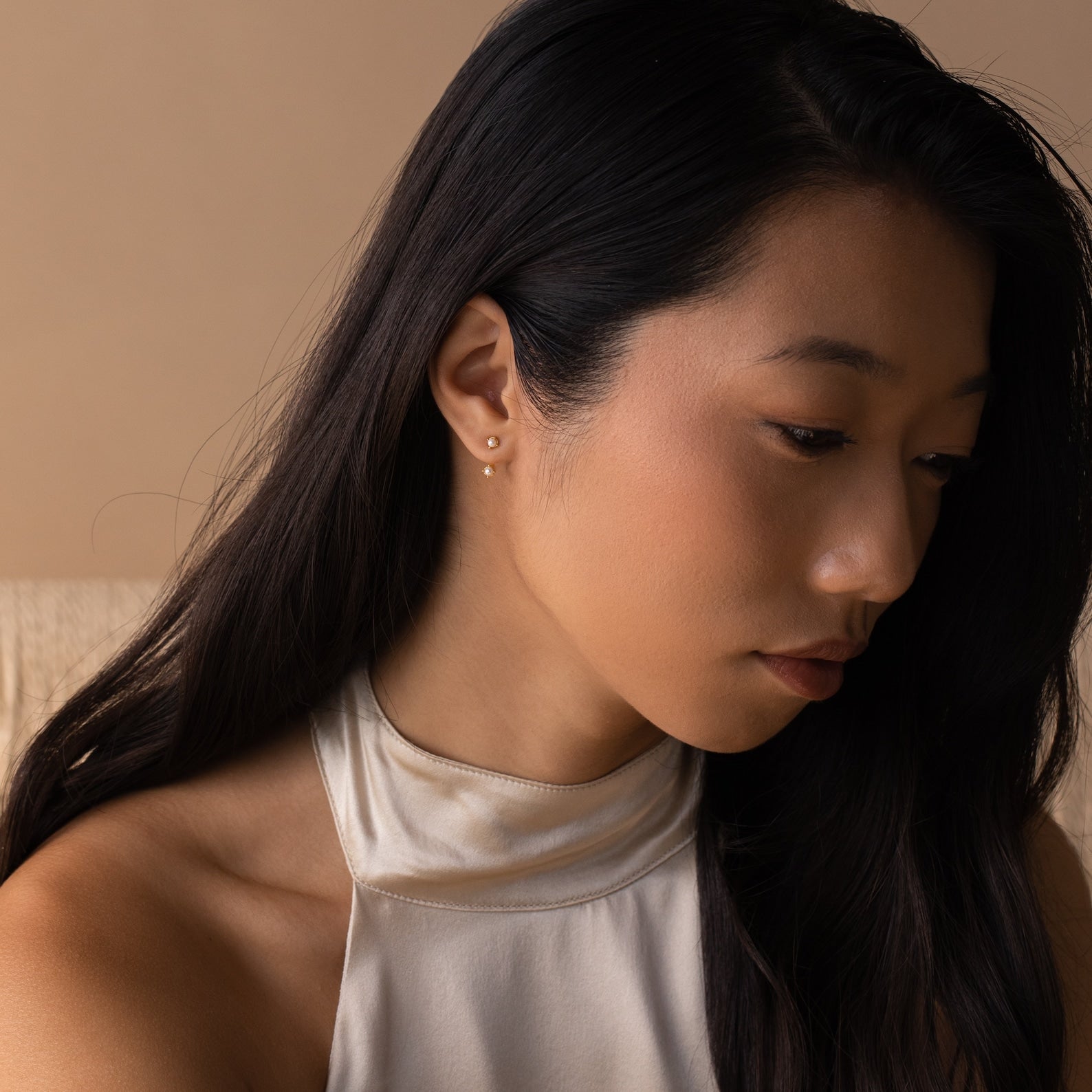 Lifestyle portrait of a woman wearing one birthstone pearl ear jacket in her lobe, styled with a white halter top.