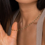 A woman delicately holds the Evergreen Necklace Set near her neck, its small green beads glinting softly.