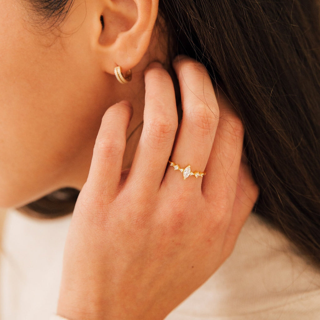 A woman touches her hair, wearing the Harlow Diamond Ring and a small gold hoop earring.
