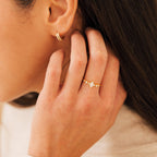A woman touches her hair, wearing the Harlow Diamond Ring and a small gold hoop earring.