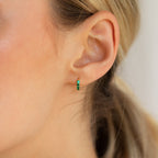 Close-up of a woman's ear wearing the Elise Gemstone Huggies Set—artisan-made small gold hoops adorned with green gemstones.