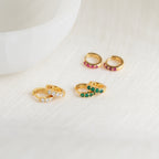 The Elise Gemstone Huggies Set features three pairs of small gold artisan-made earrings, each adorned with white, green, and pink gemstones—perfect for adding a delicate birthstone touch to any look.