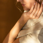 A woman rests her chin on her hand, wearing the Lovely Bracelet (CM x Lovely Bride) and light-colored clothing under soft lighting.
