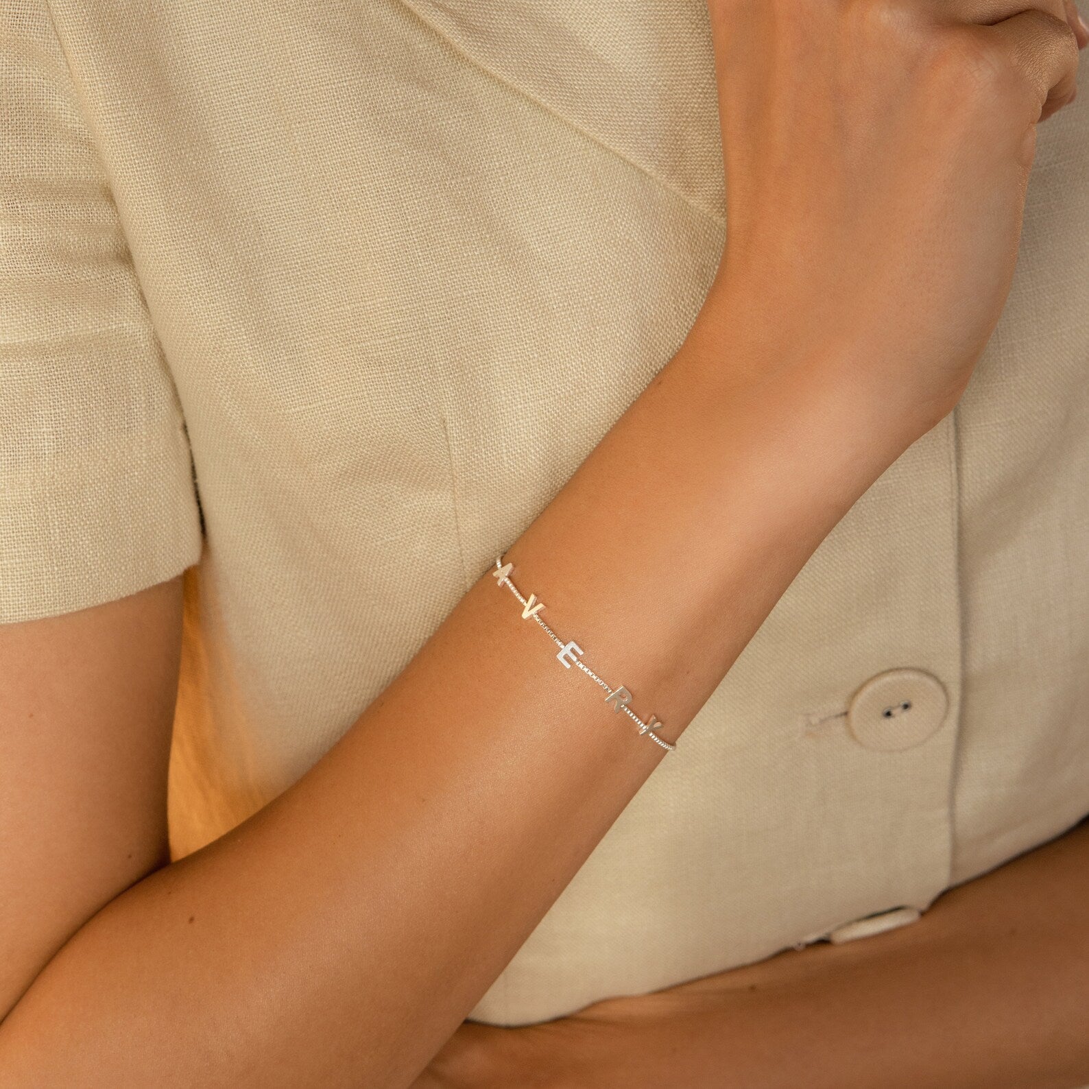 A woman wears a cream short-sleeve jacket and the Lovely Bracelet (CM x Lovely Bride) with silver letter charms on her wrist.