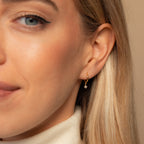 Close up of a woman's ear adorned with Molly Pearl Huggies in 18K Gold.