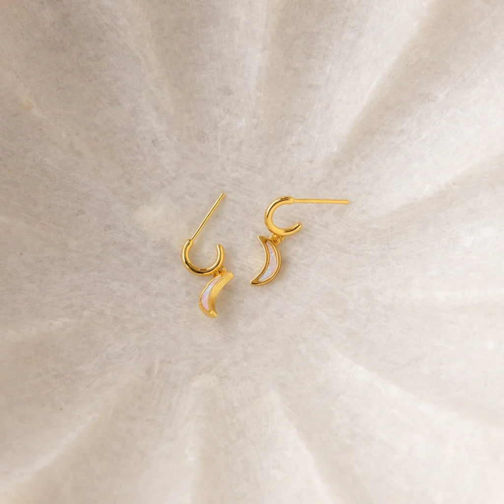 The Opal Drop Earrings Set features gold crescent-shaped earrings with delicate opal accents, displayed on a soft, light-textured background—ideal for layering with other jewelry pieces.
